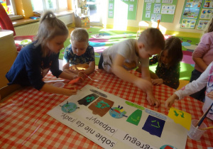 Piątka dzieci nakleja kolorowe elementy na grupowy plakat ekologiczny.